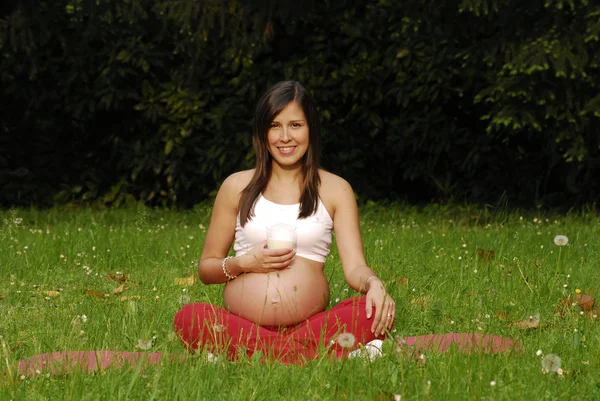 Hermosa mujer embarazada bebiendo leche y relajándose en el parque . — Foto de Stock