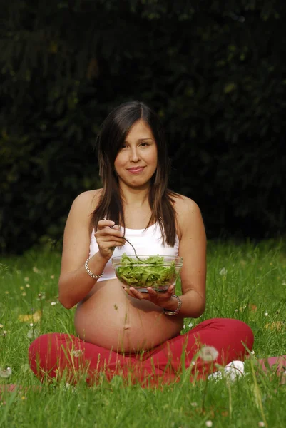 Schöne schwangere Frau isst Salat und entspannt sich im Park. — Stockfoto