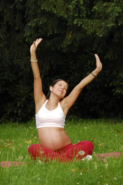 Unga gravid kvinna stretching och koppla av på en gräs. — Stockfoto