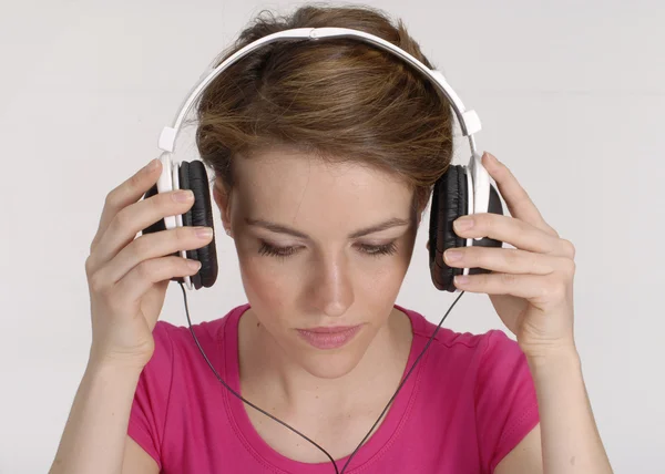 Mujer joven escuchando música y sosteniendo unos auriculares . —  Fotos de Stock