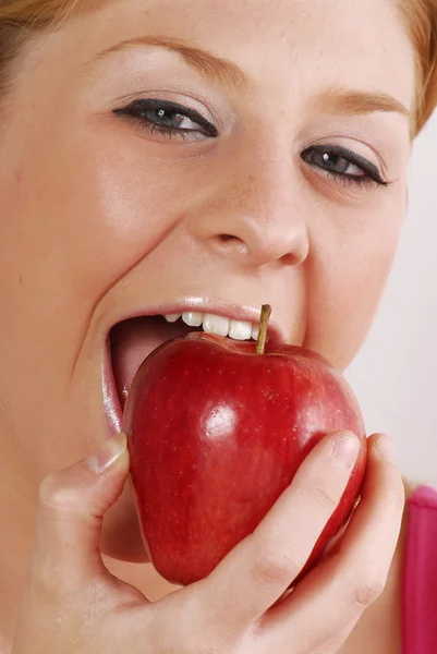 Jonge blonde vrouw die een rode appel eten. — Stockfoto