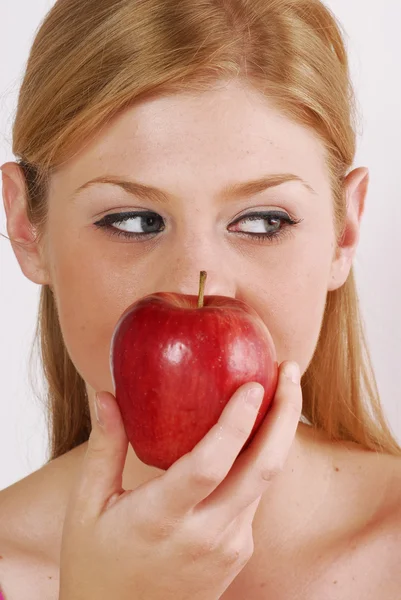 Jonge blonde vrouw die een rode appel eten. Stockafbeelding