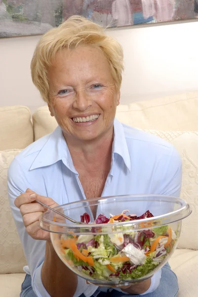 Happy senior woman eating a fresh vegetable salad at home. — Stock Photo, Image