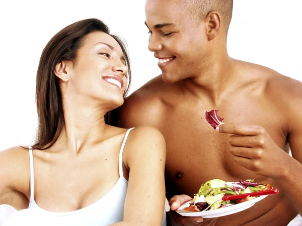 Jovem casal hispânico desfrutando e comendo salada de legumes no fundo branco . — Fotografia de Stock