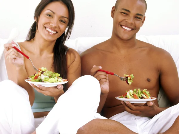 Jovem casal hispânico desfrutando e comendo salada de legumes no fundo branco . — Fotografia de Stock
