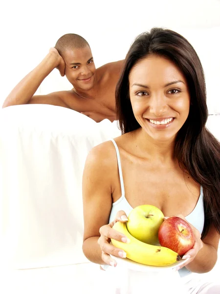 Joven pareja hispana disfrutando y comiendo ensalada de frutas en la cama . — Foto de Stock