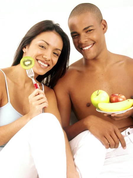Joven pareja hispana disfrutando y comiendo ensalada de frutas en la cama . — Foto de Stock