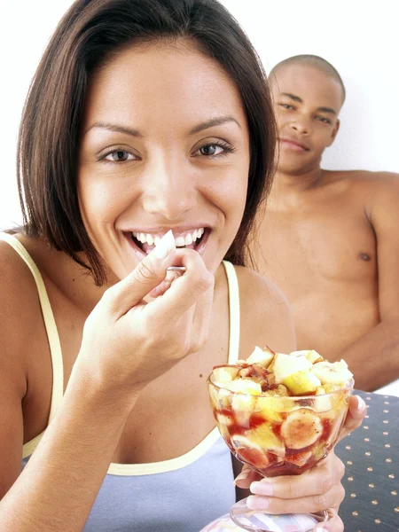 Jeune couple hispanique profiter et manger de la salade de fruits sur le lit . — Photo