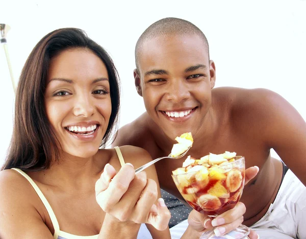 Junges hispanisches Paar genießt und isst Obstsalat auf dem Bett. — Stockfoto