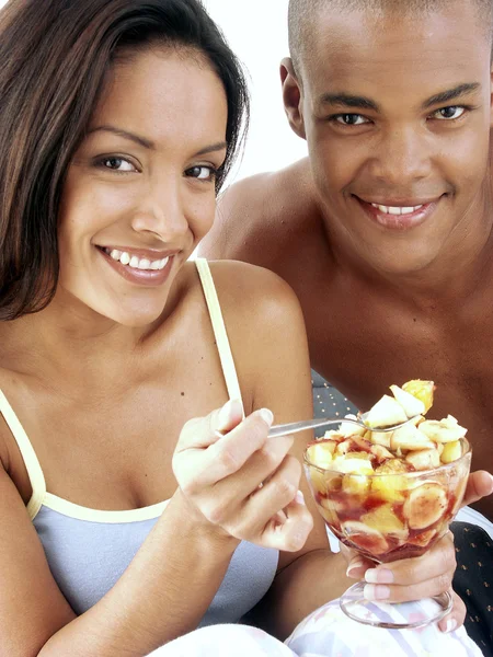 Young hispanic couple enjoying and eating fruit salad on bed. — Stock Photo, Image