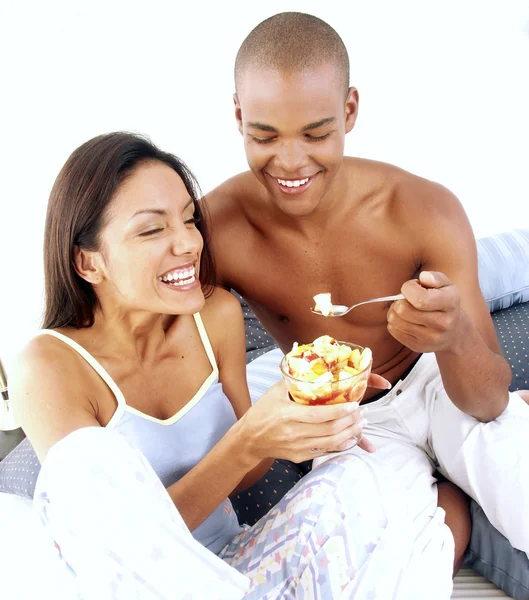 Young hispanic couple enjoying and eating fruit salad on bed. — Stock Photo, Image