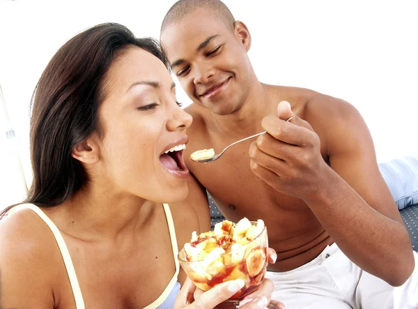 Jovem casal hispânico desfrutando e comendo salada de frutas na cama . — Fotografia de Stock