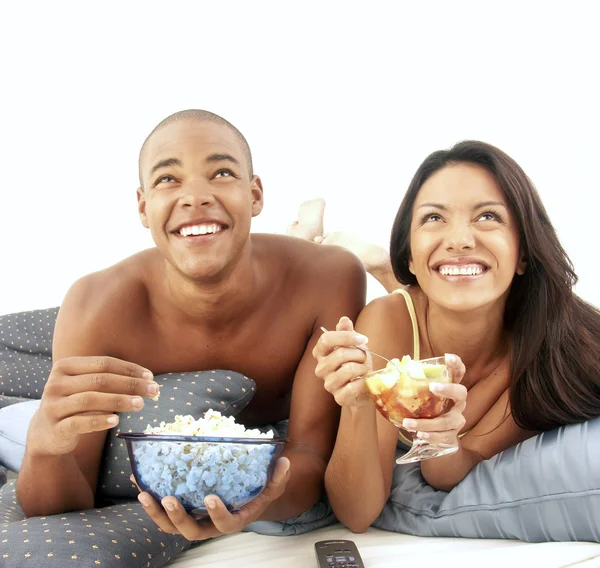 Jovem casal hispânico desfrutando e comendo salada de frutas na cama . — Fotografia de Stock