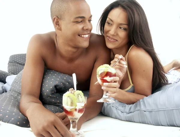 Young hispanic couple enjoying and eating fruit salad on bed. — Stock Photo, Image