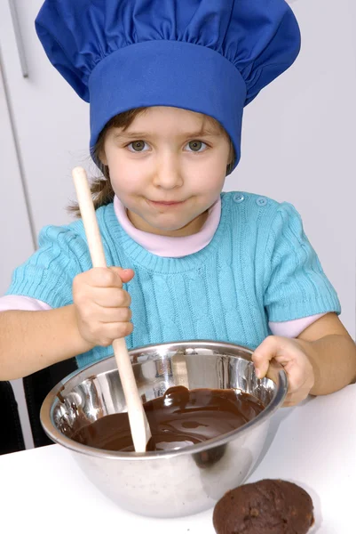 Little girl cooking chocolate in a kitchen.Little girl using a chef cap and cooking in a kitchen. — Stock Photo, Image