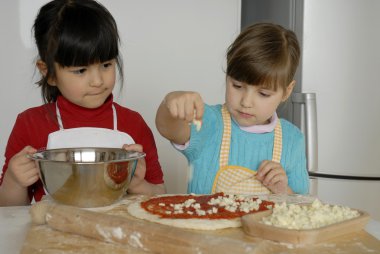 iki küçük kız birlikte kitchen.little çocuk bir mutfakta pizza pişirme.
