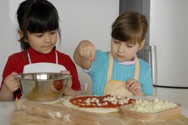 iki küçük kız birlikte kitchen.little çocuk bir mutfakta pizza pişirme.