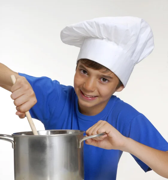 Bambino che cucina su una padella metallica con in mano un cucchiaio, cuoco che cucina, cuoce i bambini . — Foto Stock