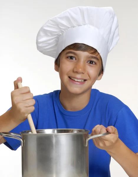 Bambino che cucina su una padella metallica con in mano un cucchiaio, cuoco che cucina, cuoce i bambini . — Foto Stock