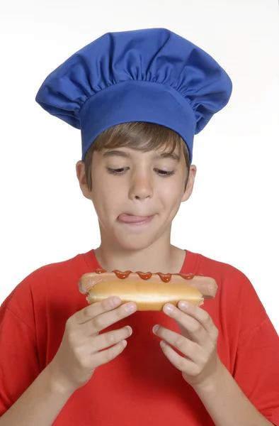 Chef pequeño niño sosteniendo hotdog, niño comiendo hotdog . — Foto de Stock