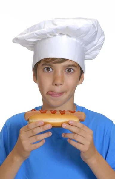 Piccolo chef con in mano hotdog, ragazzo che mangia hotdog . — Foto Stock