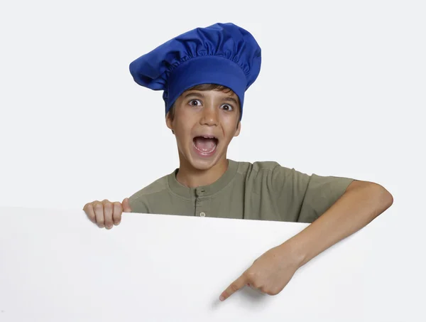 Pequeno chef criança segurando um painel branco no fundo branco . — Fotografia de Stock