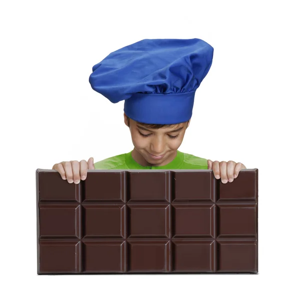 Kleiner Junge Koch hält einen großen Schokoriegel, kleines Kind hält Schokolade. — Stockfoto