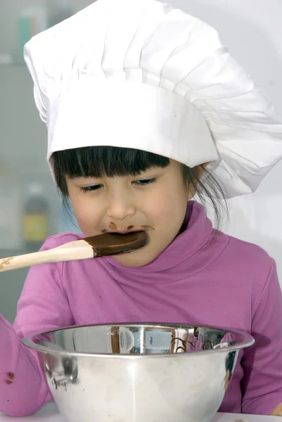 Kleines Mädchen kocht Schokolade in einer Küche.kleines Mädchen mit Kochmütze und Kochen in einer Küche. — Stockfoto