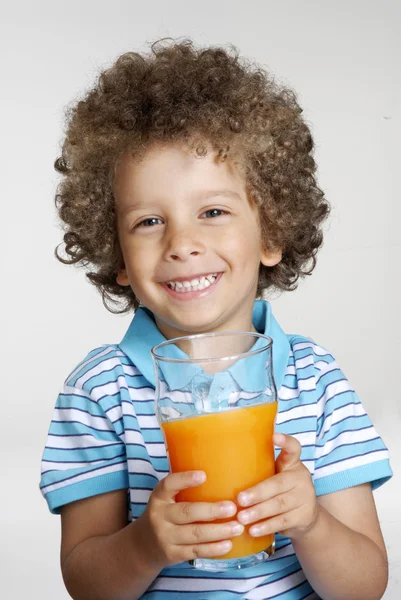 Glückliches kleines Kind hält ein Orangensaftglas in der Hand und trinkt Orangensaft. — Stockfoto