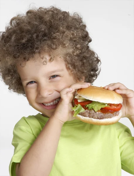 Kleines Kind hält einen großen Hamburger in der Hand und isst Hamburger. — Stockfoto