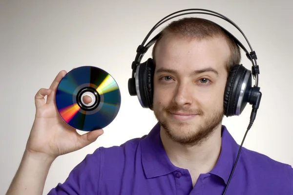 Joven disc jockey sosteniendo un disco compacto. Joven usando auriculares . — Foto de Stock