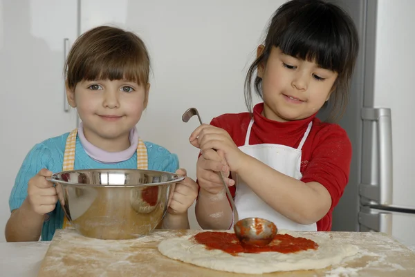 Duas meninas cozinhando uma pizza em uma cozinha.Menino em uma cozinha juntos . — Fotografia de Stock