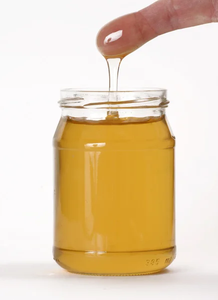 Panela de mel e um dedo no fundo branco — Fotografia de Stock