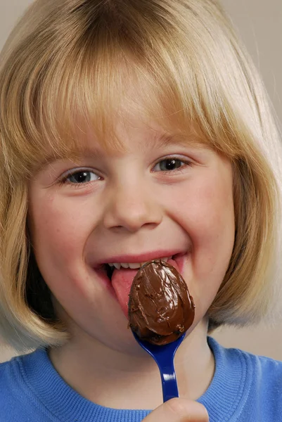 Klein meisje eten chocolade crème theelepel. — Stockfoto