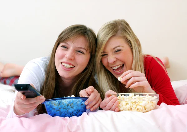 Two young women eating popcorn on bed. — Stock Photo, Image