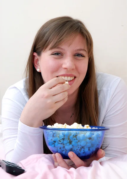 Mooie jonge vrouw genieten van eten popcorn en praten op mobiele telefoon op haar bed. — Stockfoto