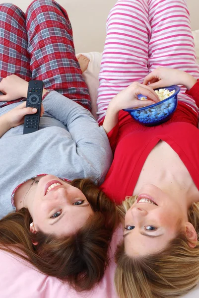 Two young women eating popcorn on bed. — Stock Photo, Image