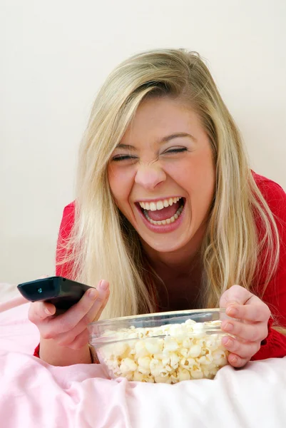 Mooie jonge blonde vrouw genieten van eten popcorn op haar bed. — Stockfoto