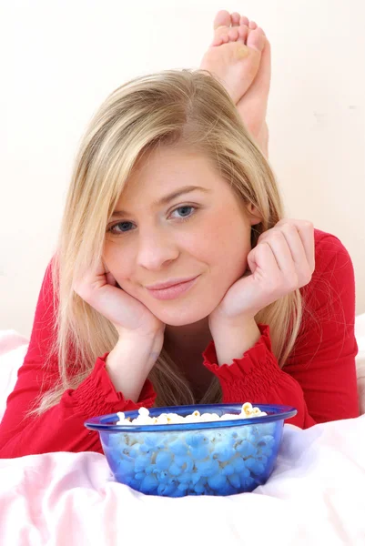 Hermosa joven rubia disfrutando comiendo palomitas de maíz en su cama . —  Fotos de Stock