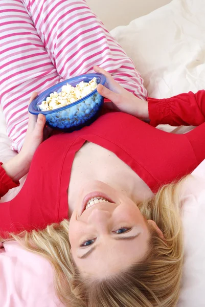 美丽年轻的金发女人享受在她的床上吃爆米花. — 图库照片