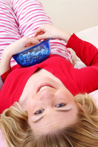 Beautiful young blonde woman enjoying eating popcorn on her bed. — Stock Photo, Image