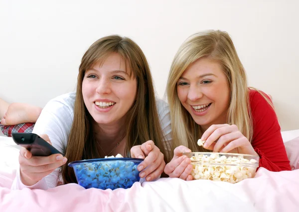 Two young women eating popcorn on bed. — Stock Photo, Image