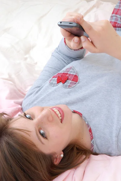 Beautiful and happy young woman portrait lying down on bed holding a tv control. — Stock Photo, Image