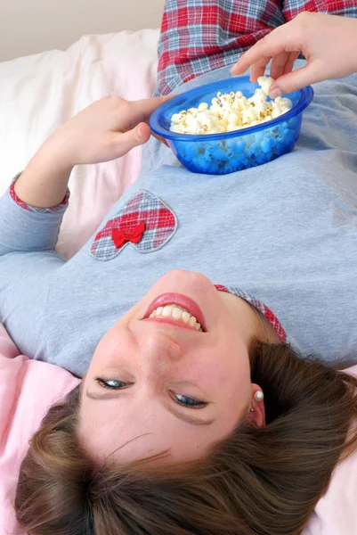 Mooie jonge Kaukasische vrouw genieten van eten popcorn op haar bed. — Stockfoto