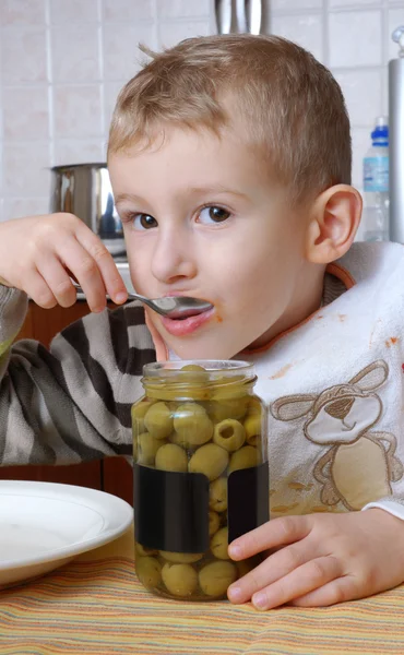 Niño comiendo aceitunas en una cocina . — Foto de Stock