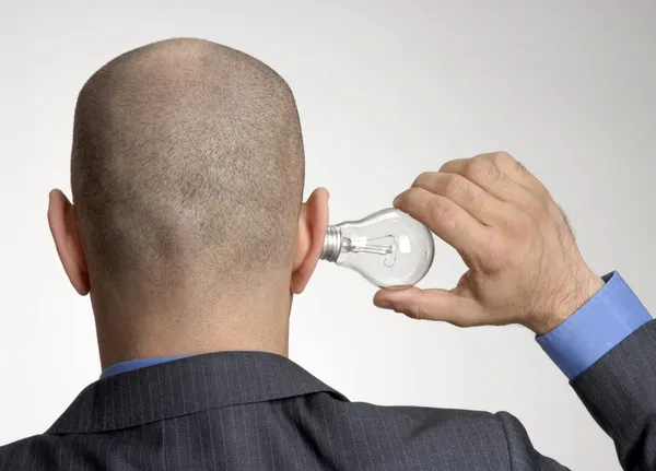 Rear view from a bald head man holding a bulb lamp on his ear. — Stock Photo, Image
