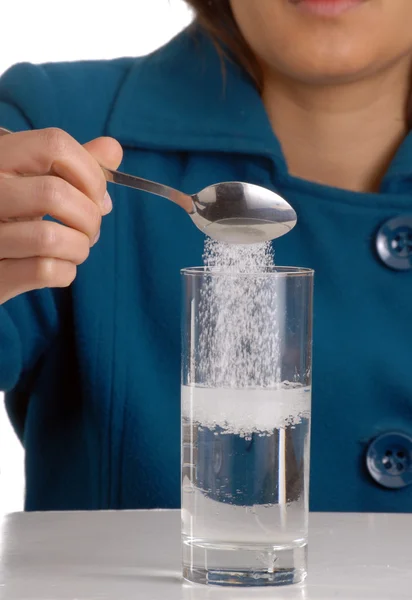 Mujer joven vertiendo azúcar en el vaso de agua . — Foto de Stock