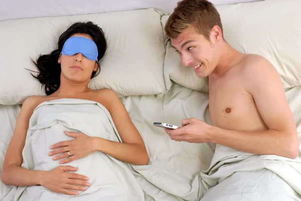 Mladý muž, chatování na mobilním telefonu v posteli — Stock fotografie