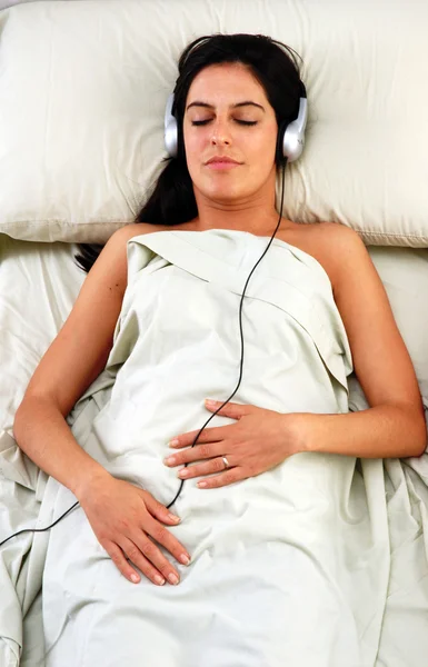 Schöne junge Frau hört Musik über Kopfhörer im Bett. — Stockfoto