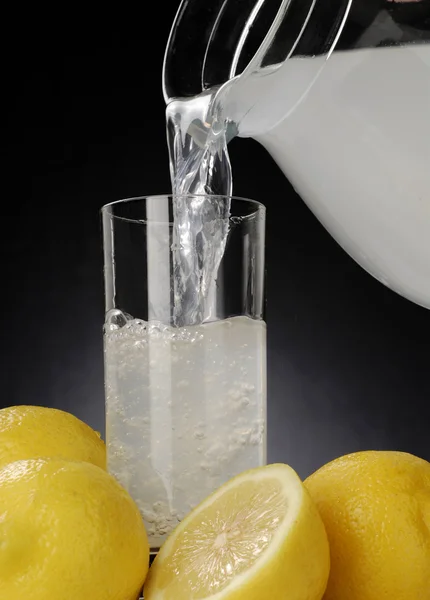 Pouring fresh lemonade glass over lemons. — Stock Photo, Image